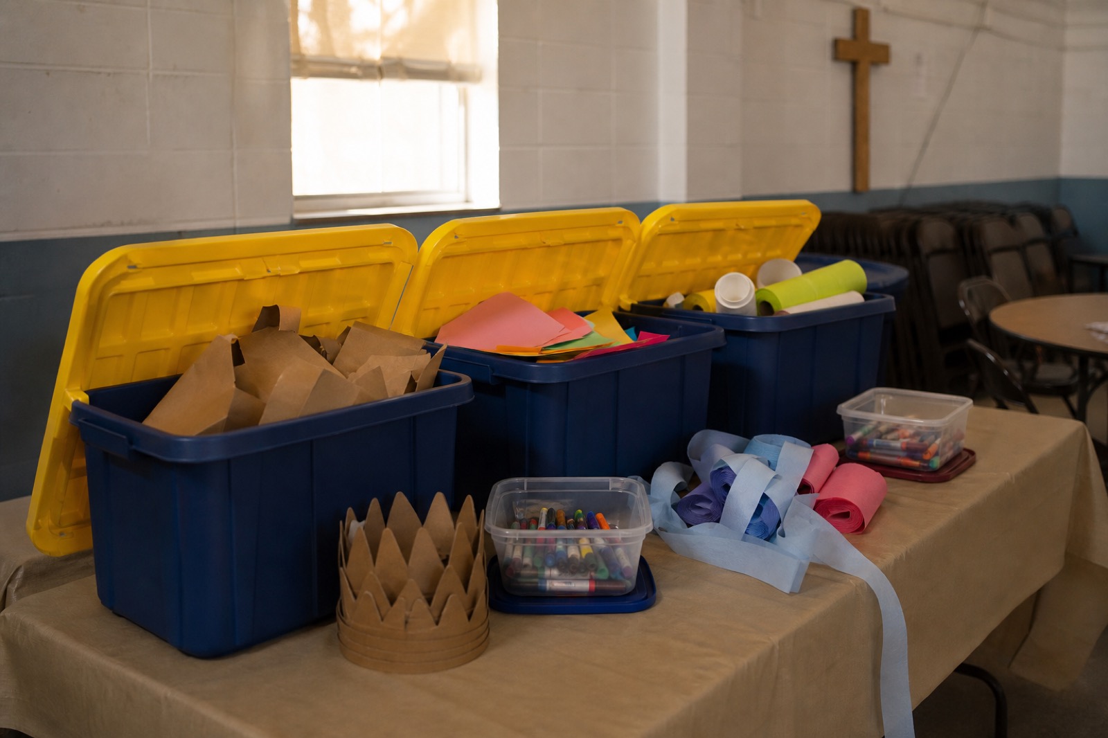 Three open ReadyTote crates on a folding table in a church fellowship hall, filled with craft paper, streamers and markers.